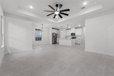 Unfurnished living room featuring ceiling fan with notable chandelier, a tray ceiling, and light tile patterned flooring