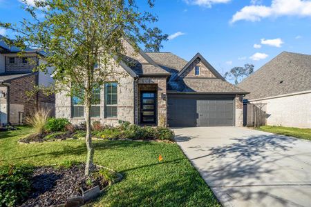 The front yard is landscaped with a neatly trimmed lawn, small shrubs, colorful plants, and a young tree in a mulched bed.