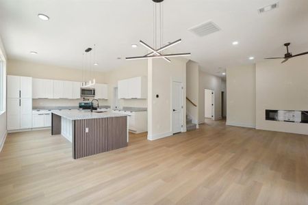 Kitchen with an island with sink, hanging light fixtures, ceiling fan with notable chandelier, white cabinetry, and light wood-type flooring