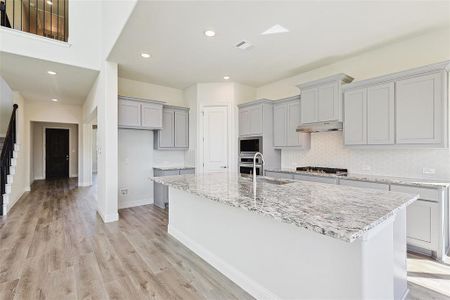 Kitchen with backsplash, an island with sink, light hardwood / wood-style floors, and stainless steel appliances