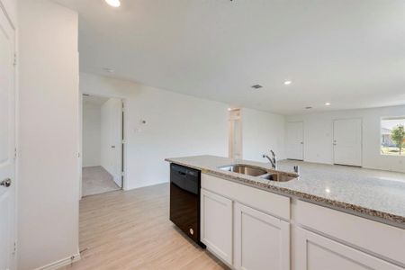 Kitchen with light wood-type flooring, white cabinets, dishwasher, light stone counters, and sink