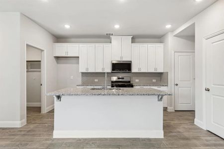 Kitchen featuring appliances with stainless steel finishes, white cabinetry, light stone counters, and an island with sink