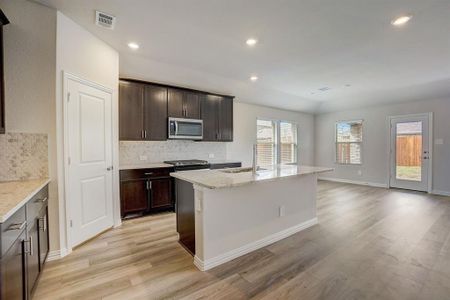 Kitchen featuring backsplash, a kitchen island with sink, light hardwood / wood-style floors, light stone countertops, and sink