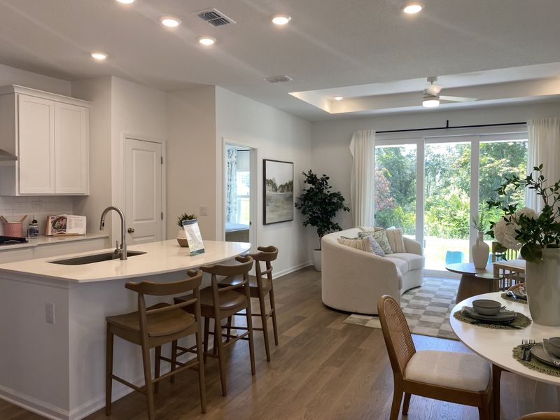 A modern open-concept kitchen and living area with sleek white cabinetry, cozy seating, and abundant natural light.