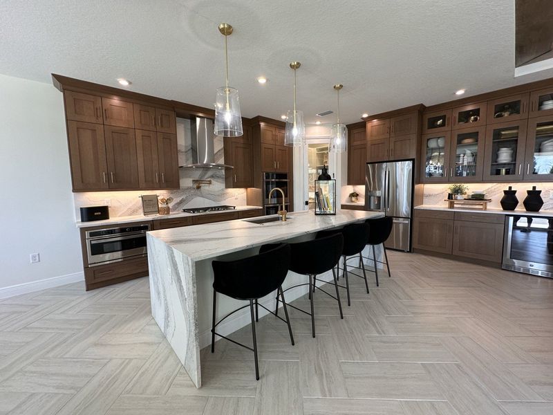 A modern kitchen with wood cabinetry, a large marble island, and elegant gold fixtures.