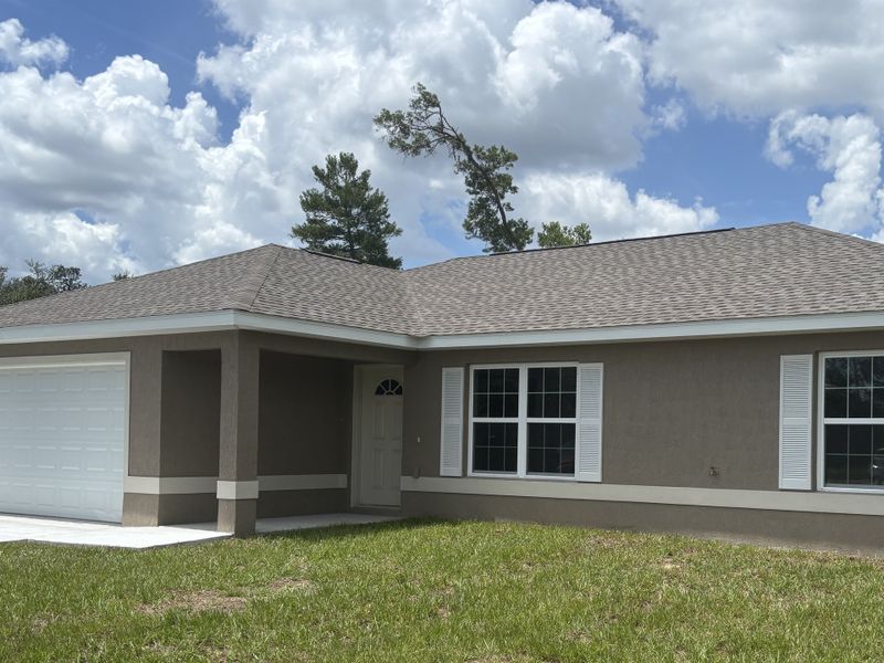 A charming beige home with white shutters and a spacious yard in Marion Oaks by Zephyr Homes (Ocala, FL).