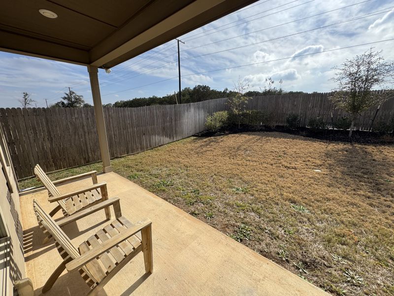 A cozy patio with wooden chairs overlooking a grassy yard and fence.