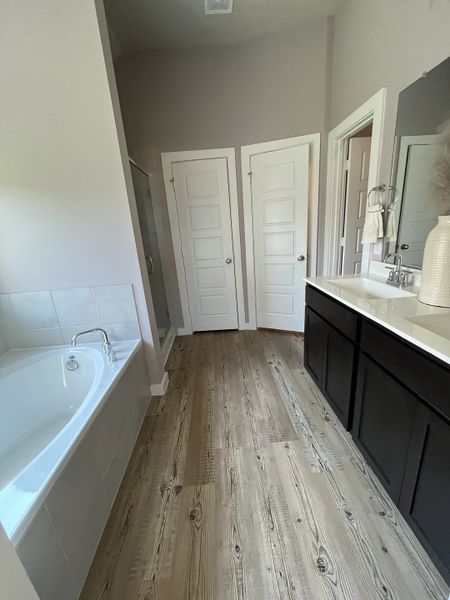 A modern bathroom featuring a sleek double vanity, elegant wood floors, and a spacious bathtub for relaxation.