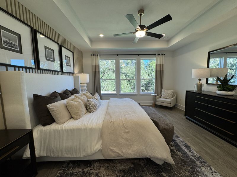 A cozy bedroom with a plush bed, elegant ceiling fan, large window, and stylish decor elements.