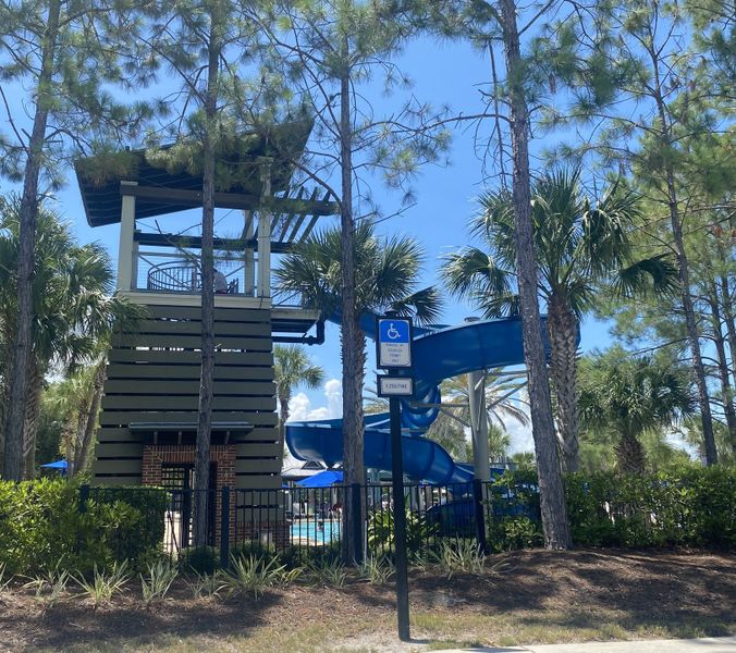 A vibrant community pool area with a towering slide surrounded by lush trees in RiverTown - Cove by Mattamy Homes (St. Johns, FL).