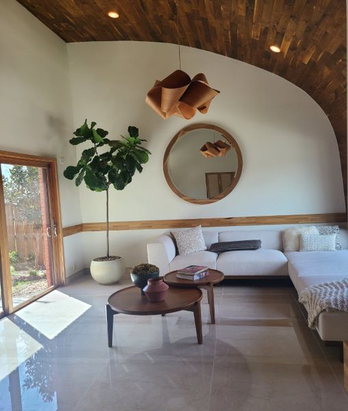 A cozy living room with wooden ceiling, white sofa, modern wood tables, and large round mirror. A cozy living room with wooden ceiling, white sofa, modern wood tables, and large round mirror.
