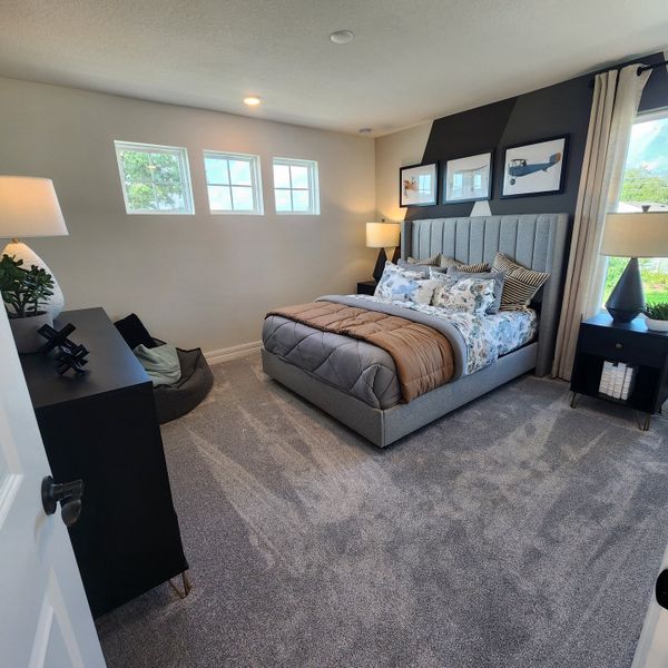 A cozy bedroom with a plush bed, modern artwork, and soft carpeting, illuminated by natural light from stylish windows.