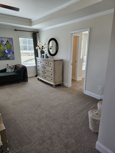 A cozy bedroom with a textured carpet, elegant dresser, and modern artwork, leading to an adjoining bathroom.