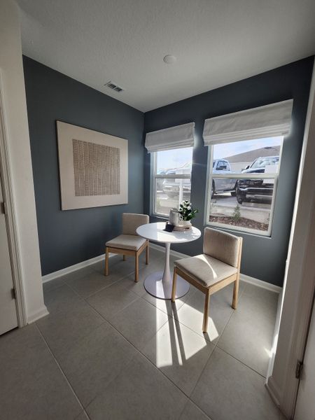 A cozy nook with a white table, modern chairs, elegant art, and natural light pouring through dual windows.
