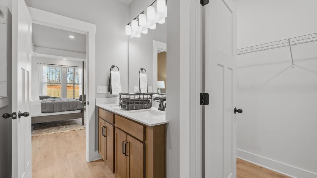 En suite primary bathroom with hardwood flooring, wood toned cabinetry, modern accents, and walk-in closet by DRB Homes En suite primary bathroom with hardwood flooring, wood toned cabinetry, modern accents, and walk-in closet by DRB Homes