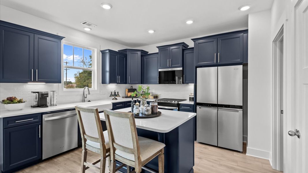 Unique, navy blue cabinetry kitchen with modern appliances and white quartz countertops at Iris Meadows by DRB Homes