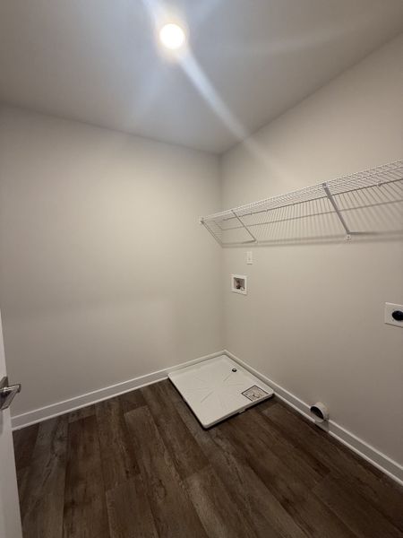 A laundry room with wood flooring, bright lighting, and a wire shelf. A laundry room with wood flooring, bright lighting, and a wire shelf.
