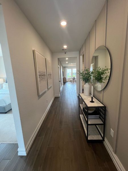 A modern hallway with wood flooring, sleek console table, circular mirror, and elegant artwork.
