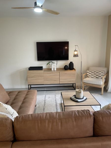 A cozy living room with a tan sofa, sleek wooden furniture, modern art decor, and a ceiling fan for comfort.