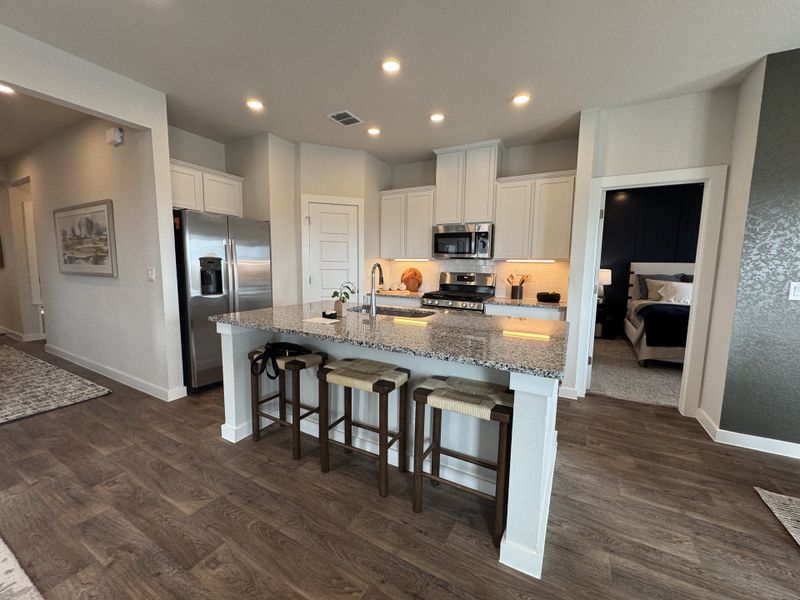 A modern kitchen with granite countertops, stainless steel appliances, and bar seating complemented by warm wood flooring. A modern kitchen with granite countertops, stainless steel appliances, and bar seating complemented by warm wood flooring.