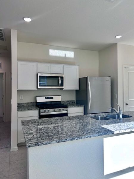 Modern kitchen with granite countertops, stainless steel appliances, and sleek white cabinetry.