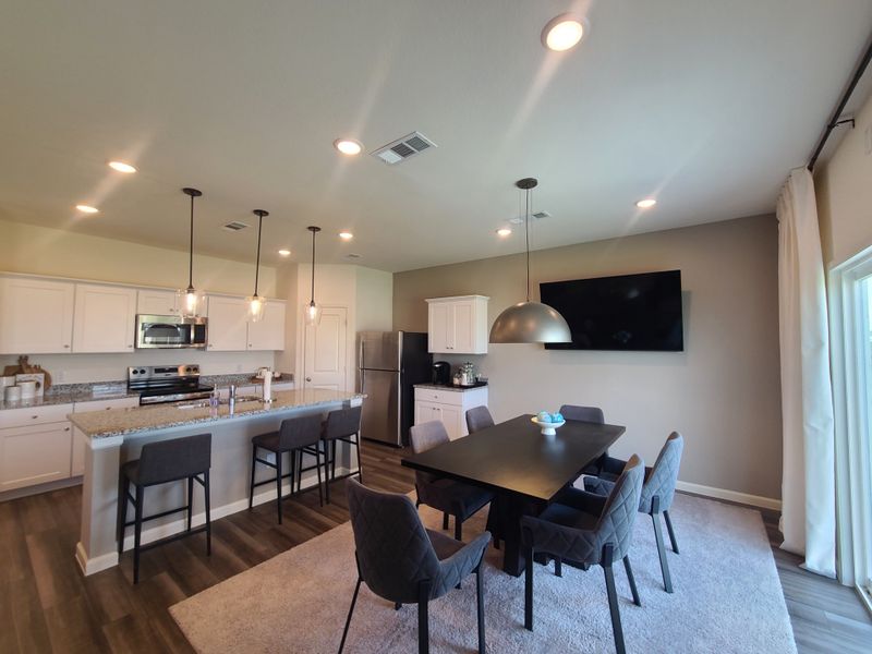 A modern kitchen with sleek lighting, granite countertops, and a spacious dining area with a stylish black table. A modern kitchen with sleek lighting, granite countertops, and a spacious dining area with a stylish black table.