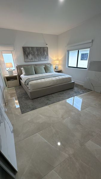 A serene bedroom with a plush bed, soft neutral decor, and glossy tiled floors, creating a cozy and modern ambiance.