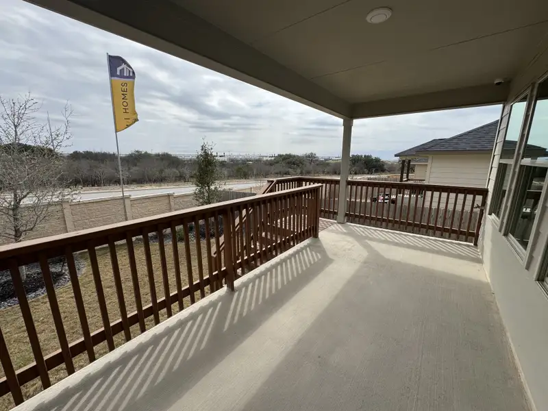A spacious covered balcony with wooden railings overlooks a yard in Hunters Ranch by M/I Homes (San Antonio, TX).