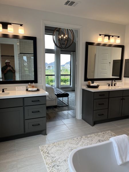 A contemporary bathroom featuring dual sinks, dark cabinetry, a modern chandelier, and elegant lighting fixtures.