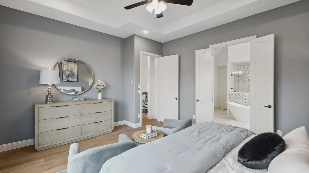Stylish bedroom with tray ceiling, light wood floors, and elegant en-suite bathroom in Westside Preserve community.