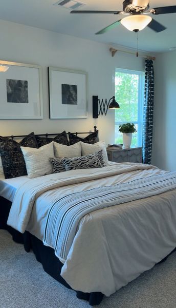 A cozy bedroom with elegant artwork, plush pillows, a striped comforter, modern lighting, and a vibrant plant by the window.