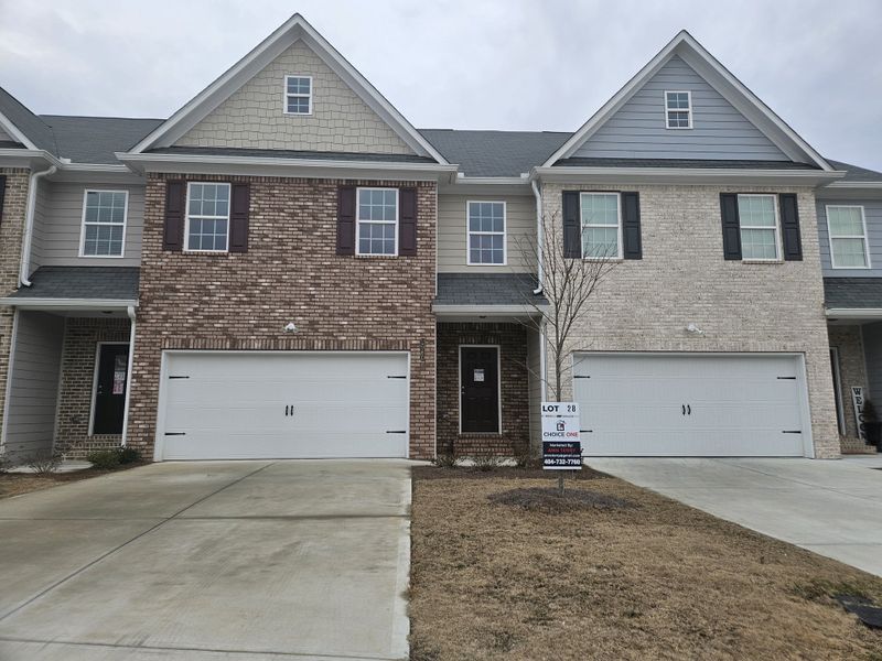 A modern brick-front townhouse with a double garage and a "For Sale" sign in a suburban neighborhood.