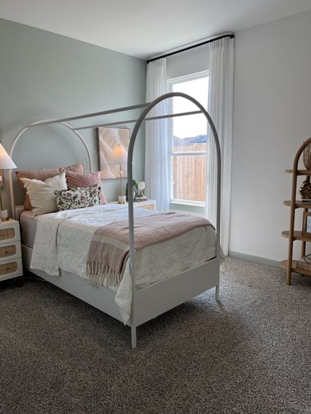 A cozy bedroom with a canopy bed, soft textiles, and elegant decor. Carpeted flooring and bright natural light.