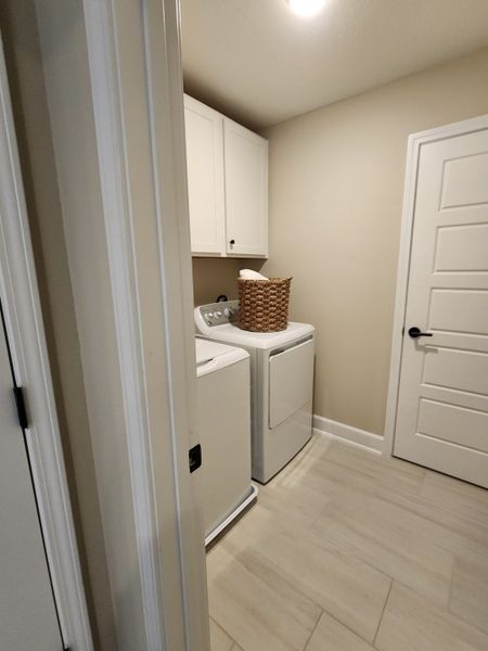 A cozy laundry room with a washer-dryer set, white cabinetry, and elegant tile flooring.