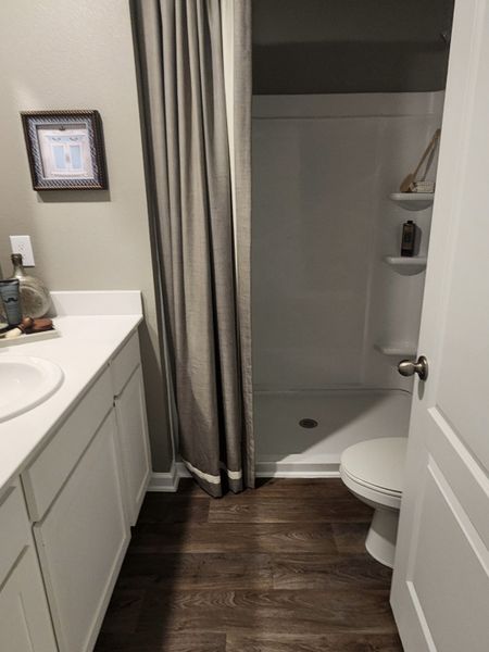A cozy bathroom featuring wood flooring, a sleek white vanity, and a curtain-enclosed shower for a touch of privacy.