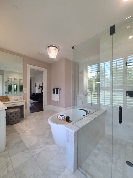 Luxurious bathroom featuring a freestanding tub, glass shower, marble tile, and elegant chandelier lighting. Luxurious bathroom featuring a freestanding tub, glass shower, marble tile, and elegant chandelier lighting.