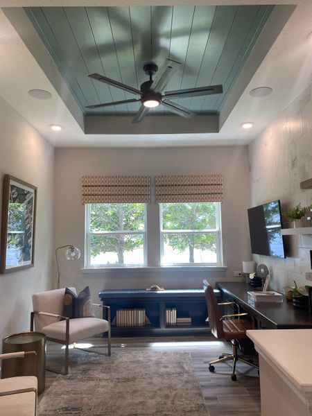 A stylish home office with a paneled ceiling, modern furniture, and abundant natural light.