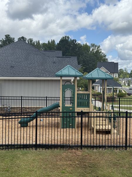 A charming playground in Poplar Preserve by D.R. Horton, Newnan, GA, featuring a slide and play structure behind a fenced area.
