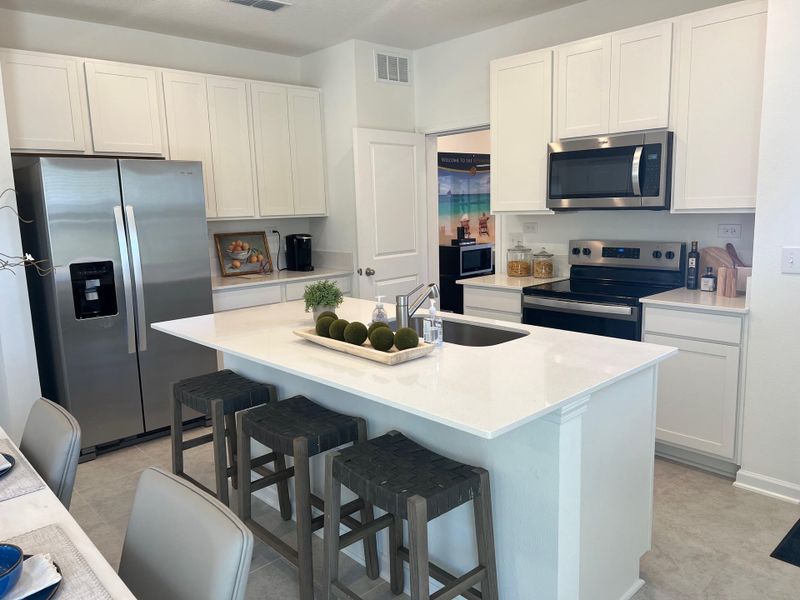A modern kitchen featuring sleek white cabinets, a stainless steel fridge, and a central island with barstools.