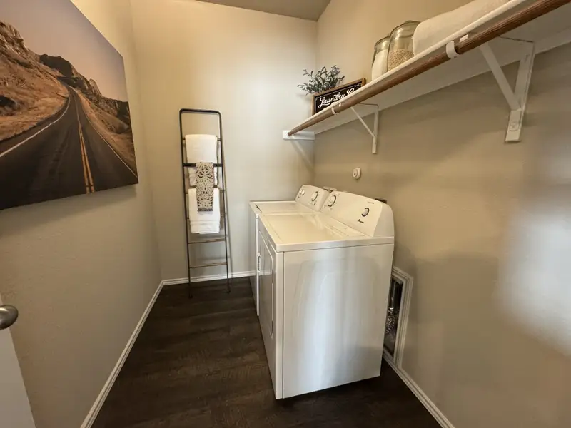 A modern laundry room with sleek appliances, dark wood flooring, and stylish shelving accessories.