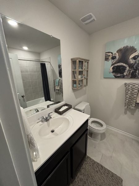 A cozy bathroom featuring a sleek vanity, tiled shower, and charming cow artwork for a rustic touch.
