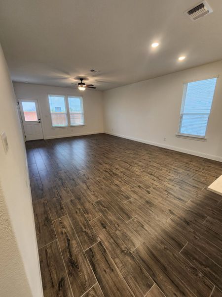 An open living area featuring wood-look flooring, large windows, and a ceiling fan for a modern touch.