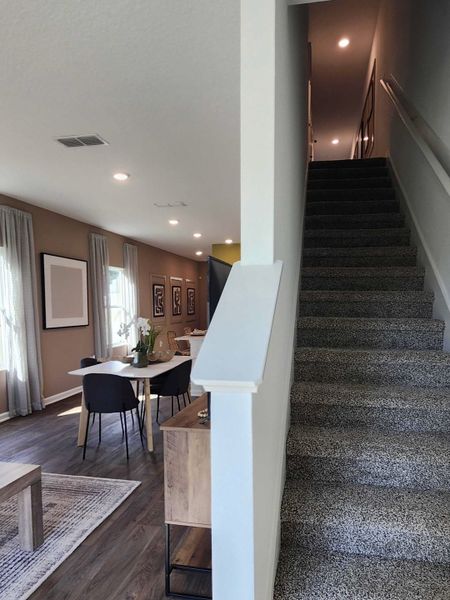 A modern interior featuring an open dining area with hardwood floors and a cozy carpeted staircase.