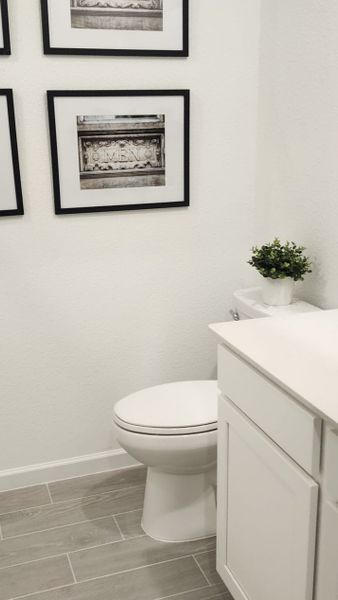 A bright powder room with a white vanity, framed wall art, and sleek tile flooring for a fresh and modern touch.