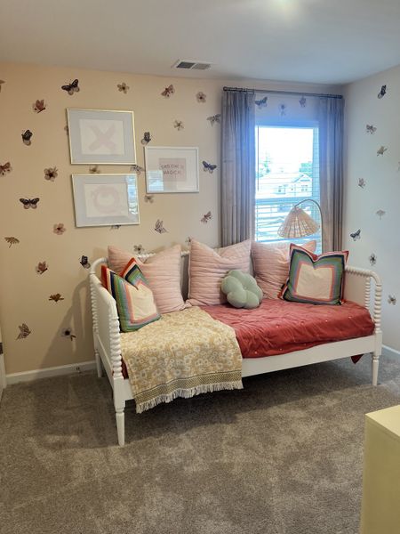 A cozy bedroom with butterfly-themed wallpaper, plush pillows, and a daybed, creating a whimsical and inviting atmosphere.