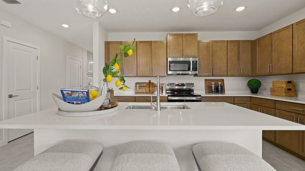 Modern Farmhouse Style Model Home Kitchen open concept Interior by DRB Homes with brown cabinets.