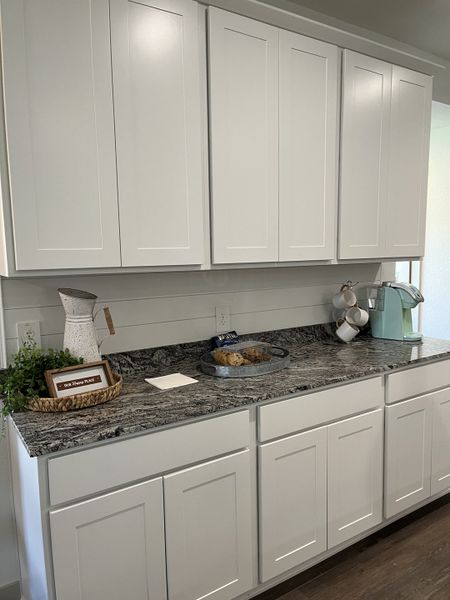 A modern kitchen with sleek white cabinets, granite countertops, and a cozy coffee corner for a stylish touch.
