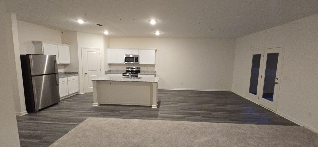 A modern kitchen with sleek appliances, white cabinetry, an island, and wood floors.