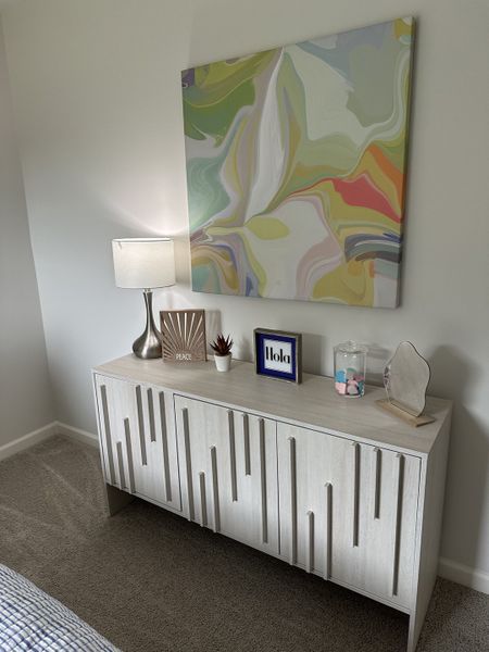 A modern dresser with artistic wood detailing, colorful abstract art, and a sleek lamp for a stylish touch.