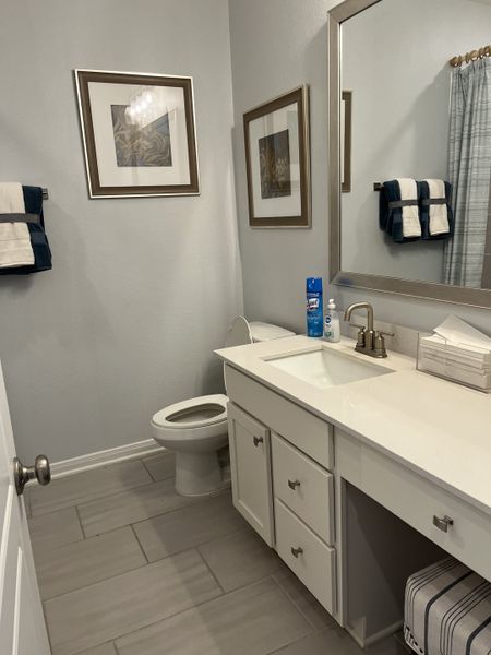 A modern bathroom featuring a sleek vanity, framed artwork, and crisp tile flooring.